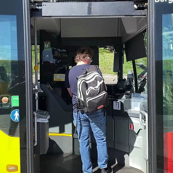 En person med ryggsäck kliver på en buss genom de öppna bussdörrarna.