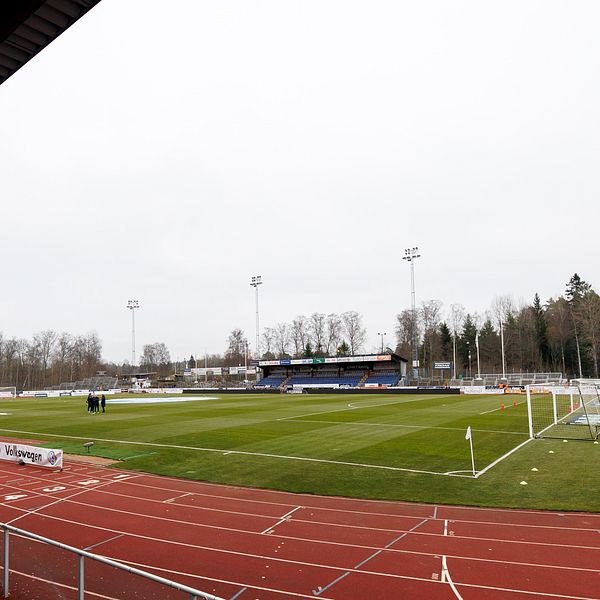 En tom fotbollsarena med gräsplan och löparbanor under en grå himmel.