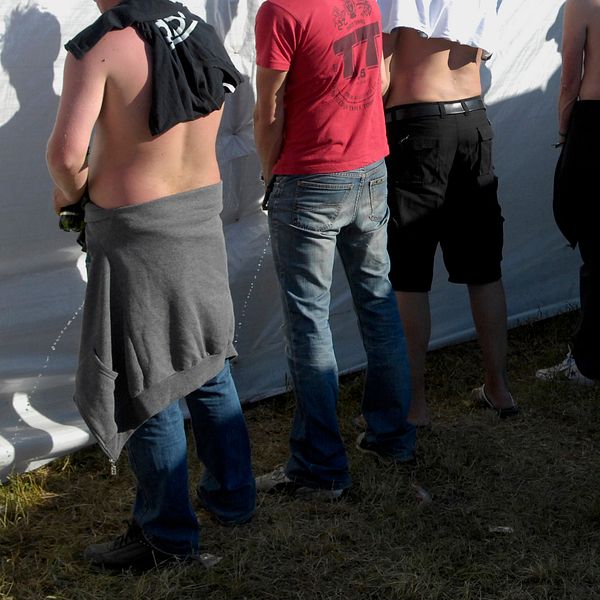 Flera killar står mot ett vitt skynke och kissar.