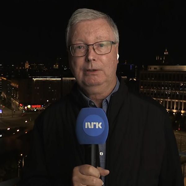 Jan Espen Kruse rapporterar för NRK med stadsmiljö i bakgrunden på kvällen.