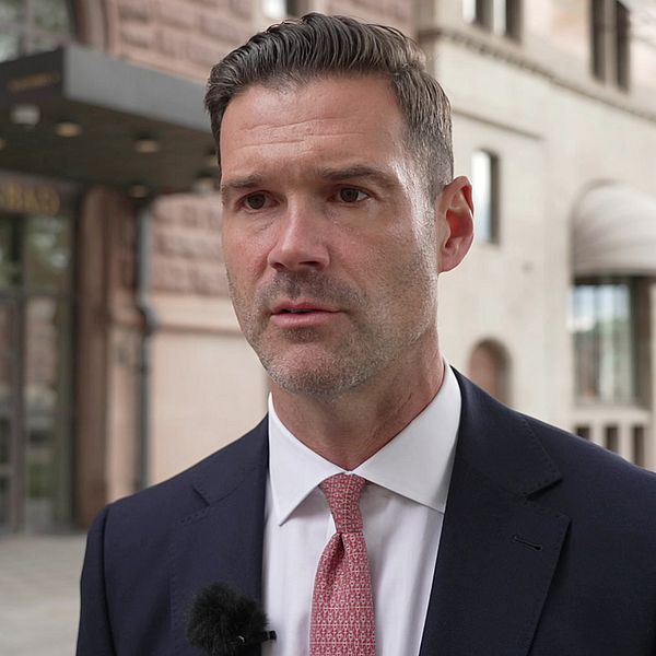 Migrationsministern och moderaten Johan Forssell har en mörk kostym, vit skjorta och ljusröd slips och ler mot kameran.