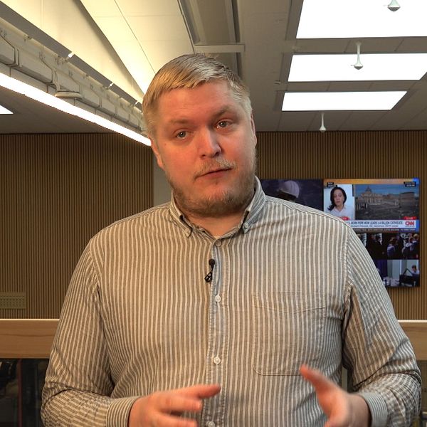 Jimmy Kirvesmäki, reporter på SVT, står talande inomhus med tv-skärmar i bakgrunden.