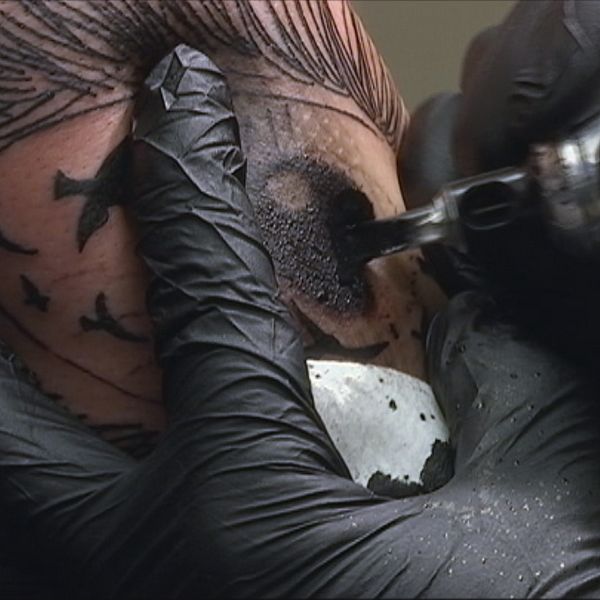 Hand med svart handske som tatuerar en arm