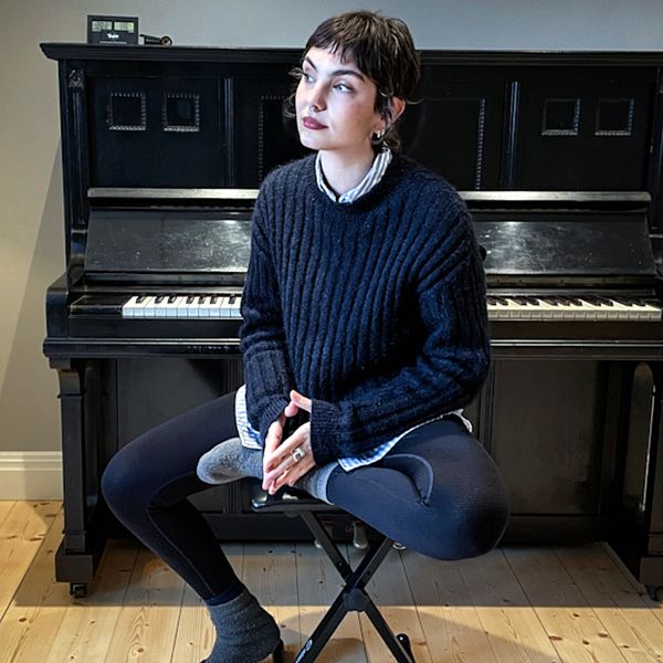 Linn Grins, artist och låtskrivare i bandet Raketklubben, sitter på en pall vid ett piano.
