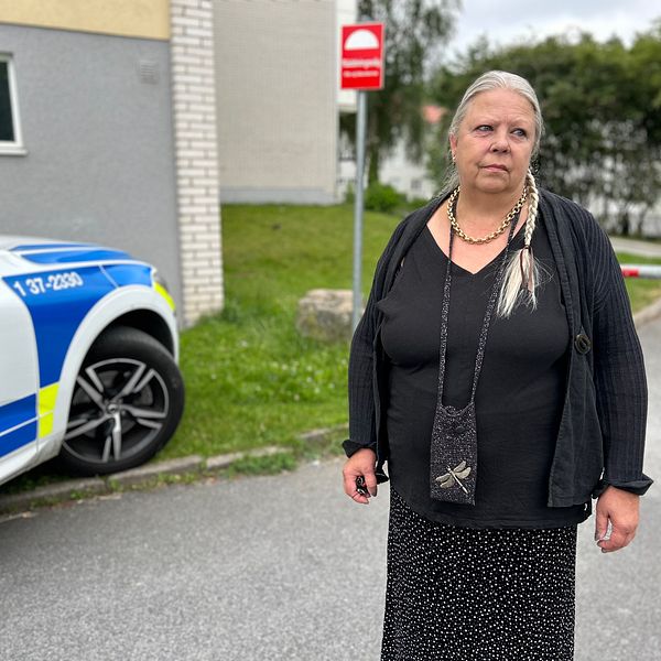 Svartklädd kvinna med håret i en fläta framför polisbil