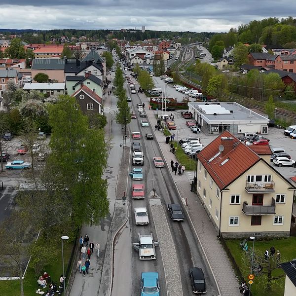Lång bilkö genom tätort, omgiven av bostadshus och bilar under molnig himmel.