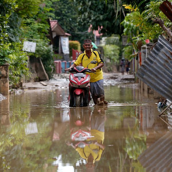 Man leder motorcykel genom översvämmat område i Indonesien 2025.
