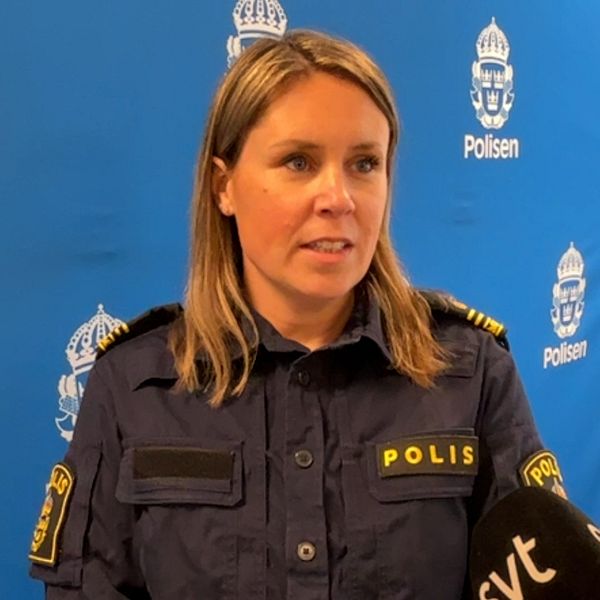 Polis i uniform intervjuas framför en blå bakgrund med polisens logotyp.