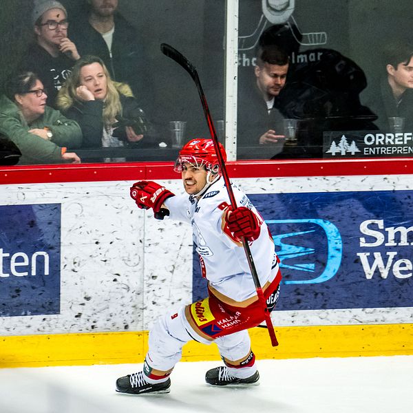 En hockeyspelare i röd och vit utrustning firar ett mål med utsträckt klubba och glädje. I bakgrunden syns åskådare vid en ishockeyrink.