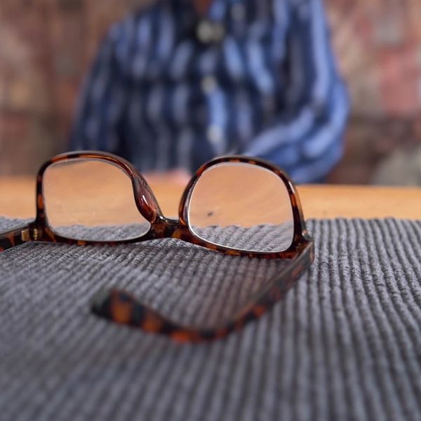 Glaslögon på ett bord framför en man som syns i oskärpa