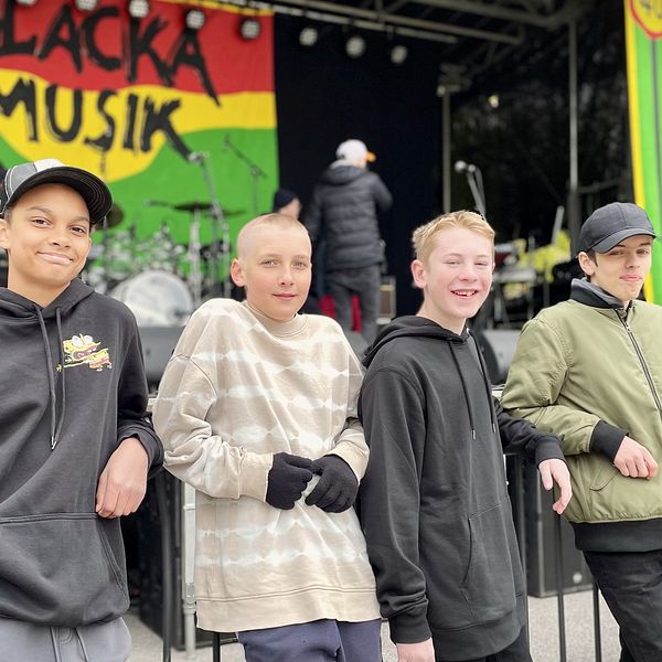 Fyra ungdomar framför en scen med banderoll där det står ”Beacka Musik”, scenfolk i bakgrunden.