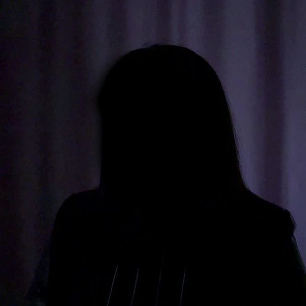 Person i mörker, ansiktet anonymiserat mot bakgrund av ljus gardin.
