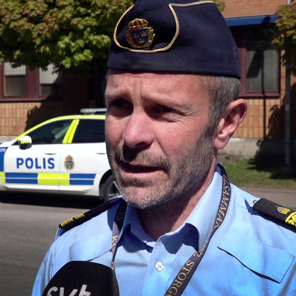 En polis ger intervju utomhus med polisbil i bakgrunden och SVT:s mikrofon synlig.