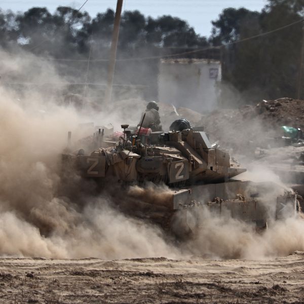 Israelisk stridsvagn vid Gazas gräns omgiven av damm och rök.