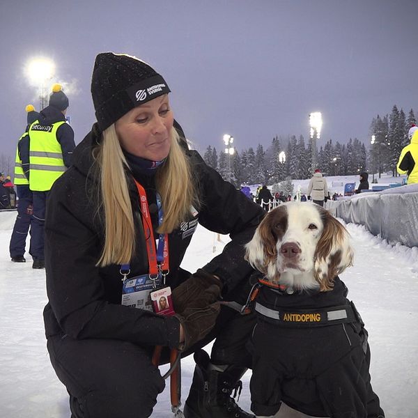 En kvinna sitter på huk på skidskyttestadion i Östersund med en hund bredvid sig.