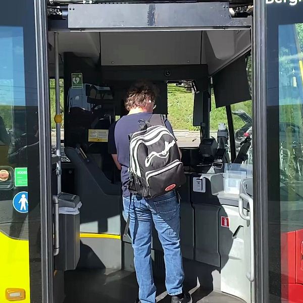 Person med ryggsäck kliver på en stadsbuss genom framdörren och visar biljett.
