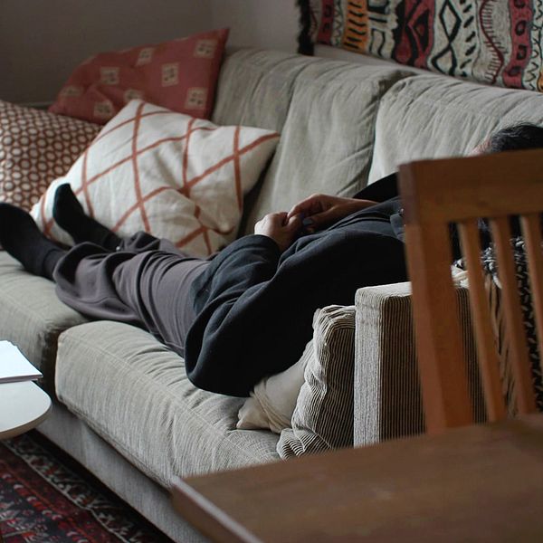 Kvinna vilar på en soffa i ett vardagsrum med kuddar och ett soffbord – och berättar om hur hon lever med konstant smärta efter en operation mot inkontinens som kallas TVT-O.