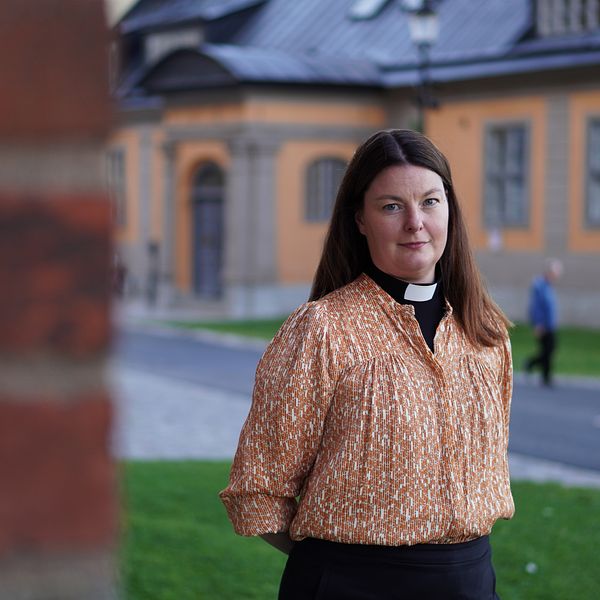 En domprost står intill domkyrkan i Uppsala, framför en gul byggnad.