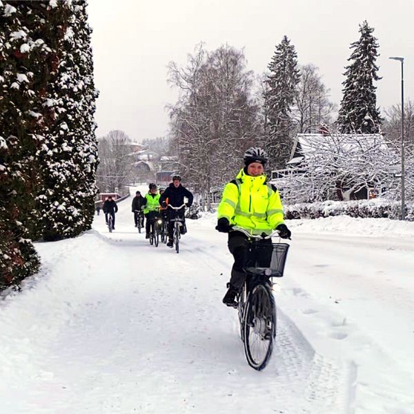 Cykelväg med snö och en kö av cyklister som cyklar mot kameran.