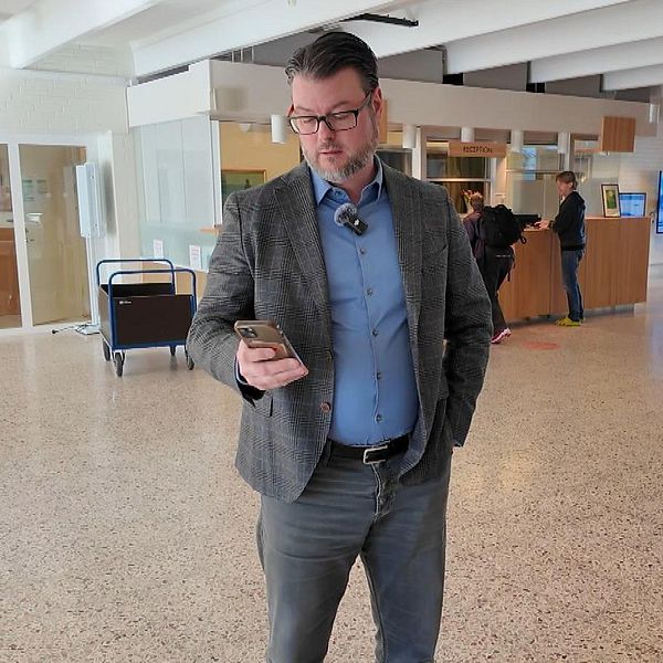 Man i kostym står i en hotellobby och tittar på sin mobiltelefon.