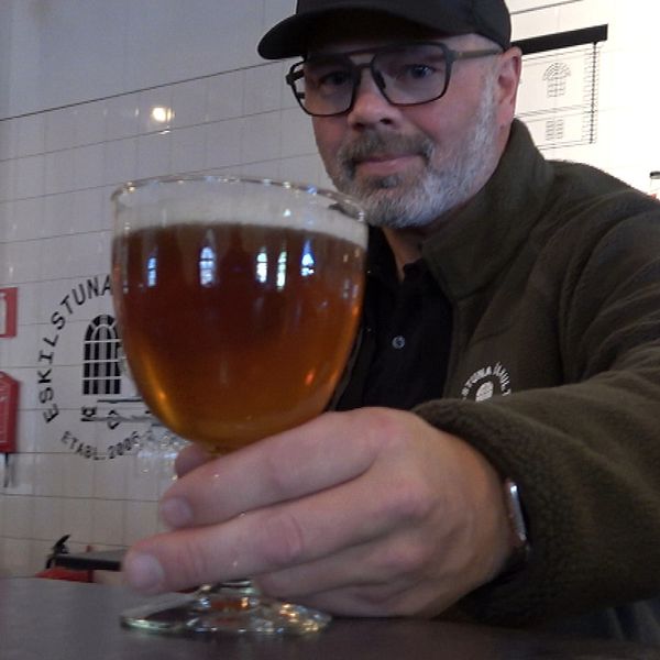 En man håller fram ett glas öl.