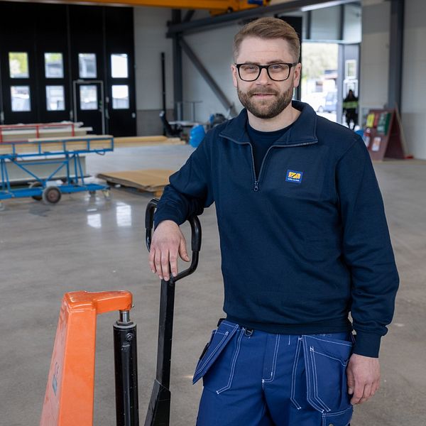 Tom Dalhqvist i arbetskläder står vid en pallvagn i en ljus industrilokal.