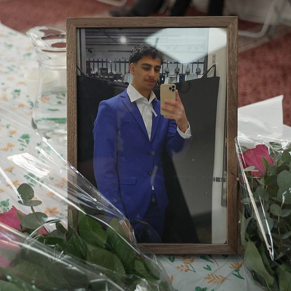 Inramat foto av en ung man, omgiven av rosor på ett blommigt bord.
