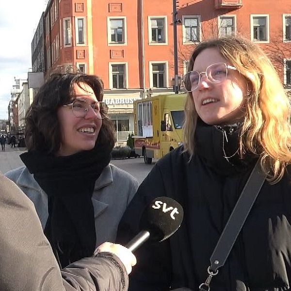 Reporter intervjuar två kvinnor på stadsgata i soligt väder.