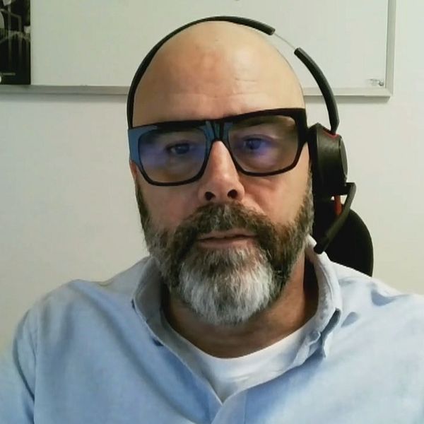 En man sitter på ett kontor med ett headset på huvudet och med en anslagstavla i bakgrunden