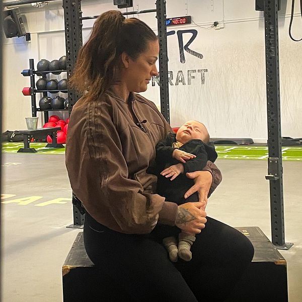 Kvinna sitter i ett gym med en bebis i famnen.