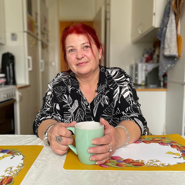 Viktoria sitter vid köksbordet och håller i en kaffemugg.