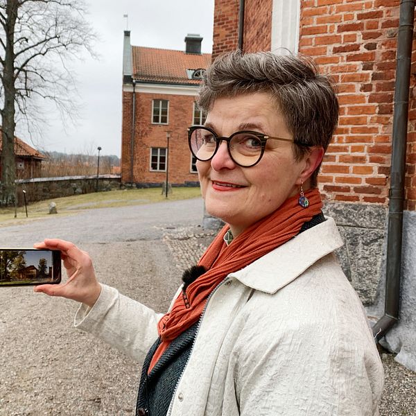 Maria Rydén Davoust står vid domkyrkan i Strängnäs. Hon håller upp en mobil med en bild.