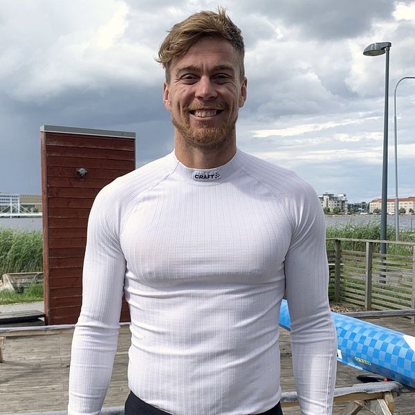 Martin Nathell står framför Munksjön, bakom honom ligger en blåvit kanot. Han har en vit långärmad tröja på sig.