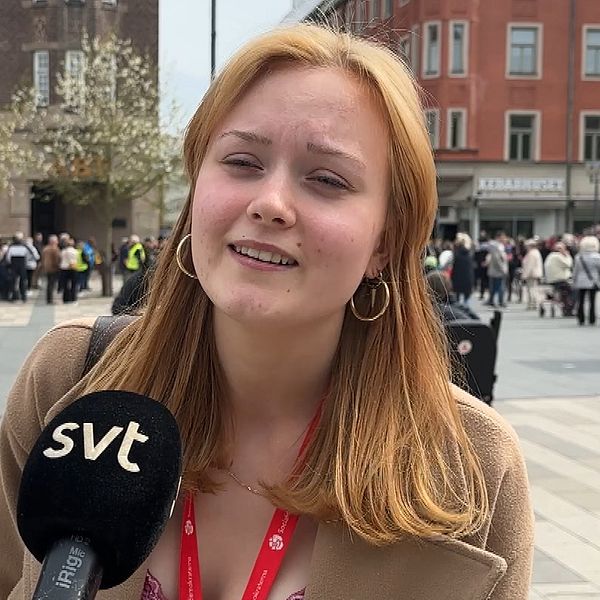 Reporter med SVT-mikrofon intervjuas på ett torg med folkmassa i bakgrunden.