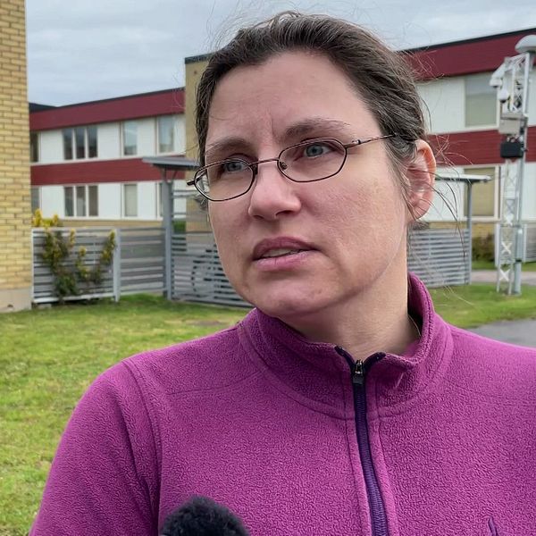 Person i lila tröja intervjuas utomhus framför en byggnad.