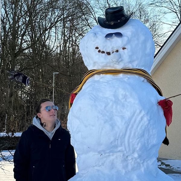 Man i villaträdgård bredvid en över två meter hög snögubbe.