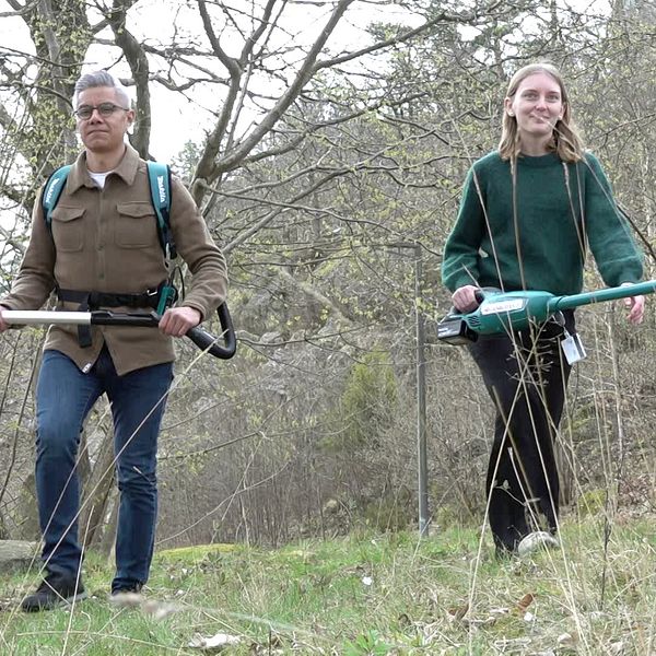 Två personer går genom en skog med bärbara dammsugare.