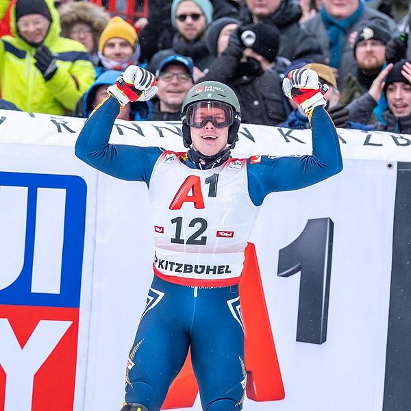 En alpinskidåkare står med segergester framför en folkmassa vid tävlingsområdet, med synlig reklamskylt för ”Liqui Moly” i bakgrunden.
