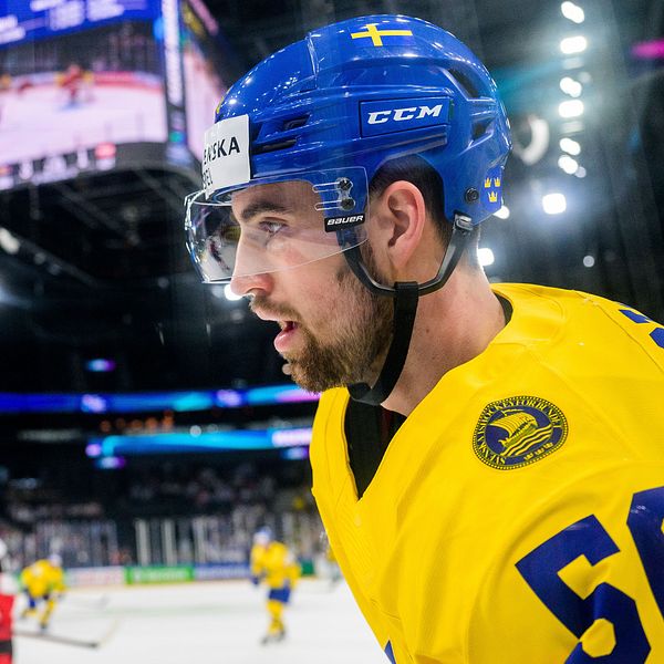 Ishockeyspelare i gul tröja på isen under match mot lag i rödvit dräkt.