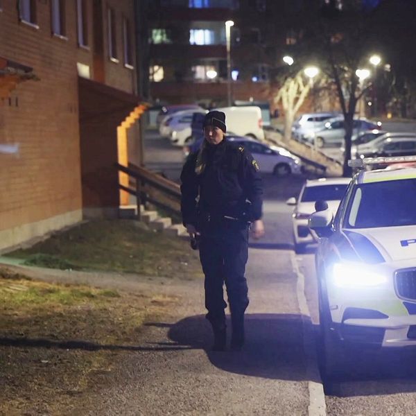 Polis går på trottoaren och flera polisbilar parkerade bredvid.