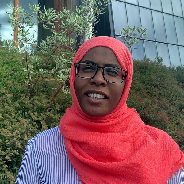 Studenten Alsiraira från Sudan står iklädd en röd sjal och glasögon på campus i Borlänge.