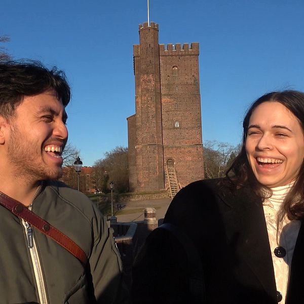 Två personer, en man och en kvinna, står framför Kärnan i Helsingborg. De skrattar och ler mot varandra.