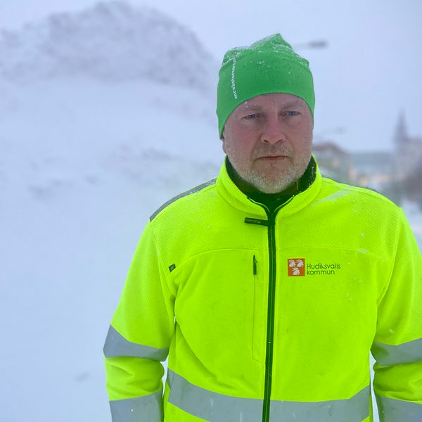 Gatuchef Peter Söderlund står iklädd Hudiksvall kommuns neonfärgade jacka. Bakom honom syns en ansenlig hög med snö.
