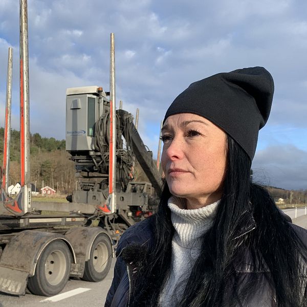 Malin Hansson står vid väg 650 där en timmerbil kör förbi.