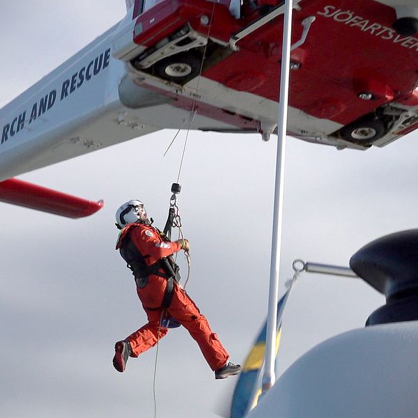en ytbärgare hänger i vajer nedanför sjöräddningshelikopter.
