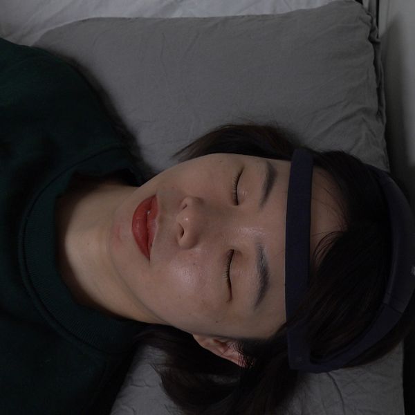 Kvinna som ligger i säng med en sensor runt huvudet
