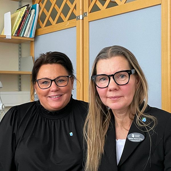 Helena Vennerström och Camilla Fermby sitter bredvid varandra i ett rum med en bokhylla i bakgrunden. De bär arbetskläder med en namnskylt synlig på den ena personens kavaj.