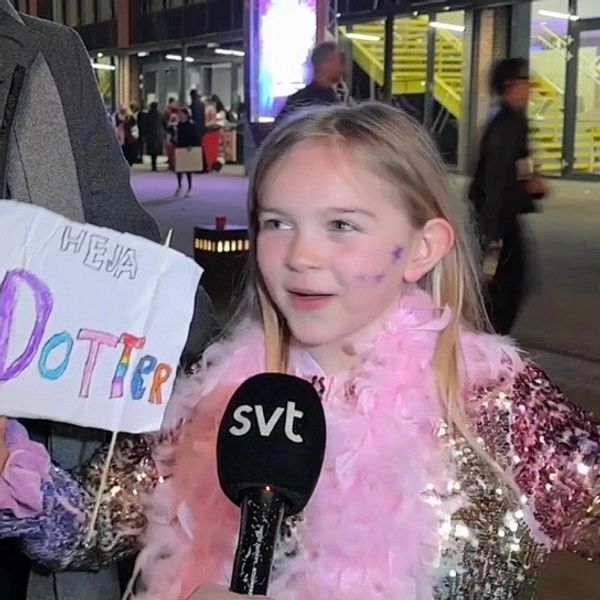 Tjej står med skylt och ser glad ut, håller upp armarna