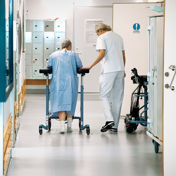 Sjuksköterska med patient i korridor på sjukhus.