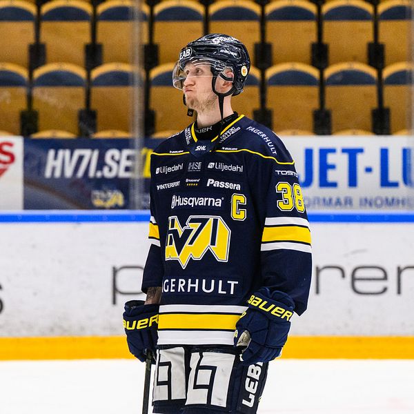 Ishockeyspelare från HV71 med hjälm och nummer 38 på tröjan står på isbanan.